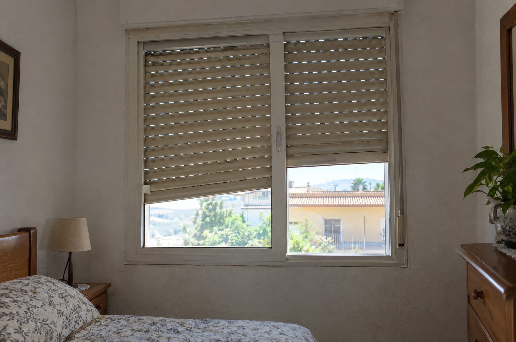 Ventana de un dormitorio con dos persianas beis de PVC bajadas a distinta altura